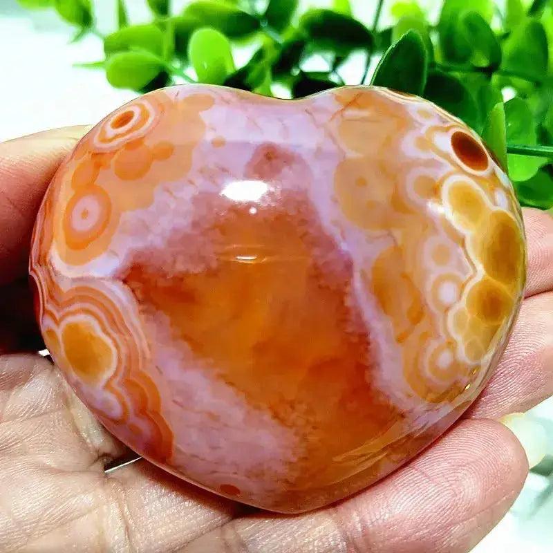 Polished Red Agate heart, a grounding vitality stone with vibrant orange, red, and white banding, held in a hand.