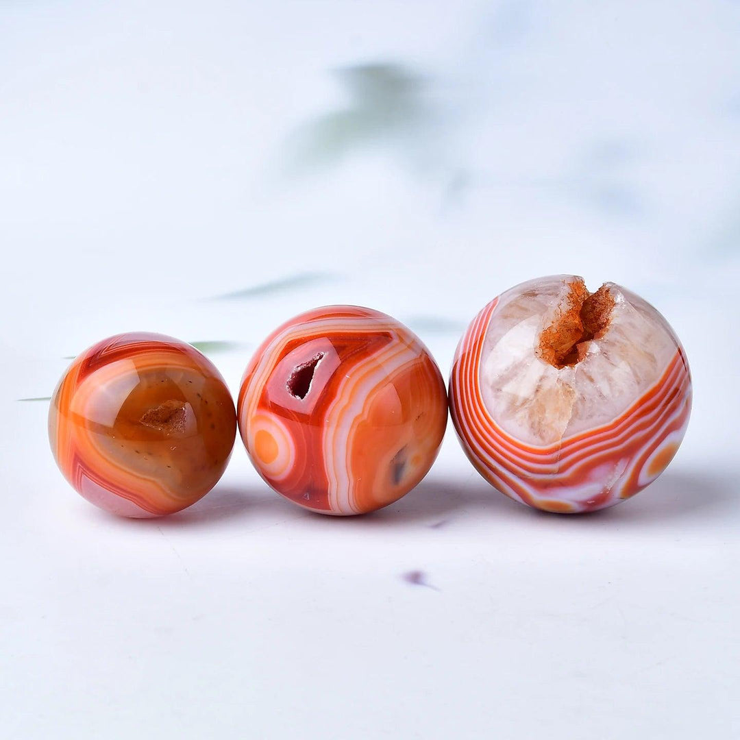 Three polished Red Banded Agate crystal spheres, showcasing deep crimson, rust, and terracotta layers with natural geodes.