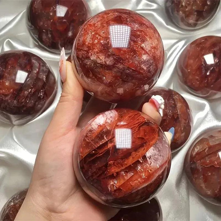 Hand holding two vibrant Red Hematoid Fire Quartz spheres with fiery red and orange inclusions, radiating passionate energy.