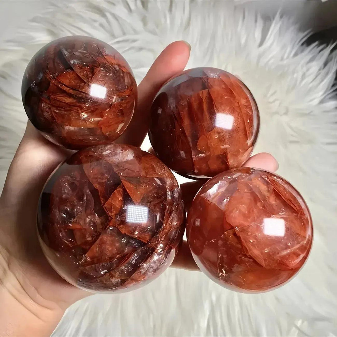 Hand holding four vibrant Red Hematoid Fire Quartz spheres with fiery red and orange inclusions, radiating passionate energy.