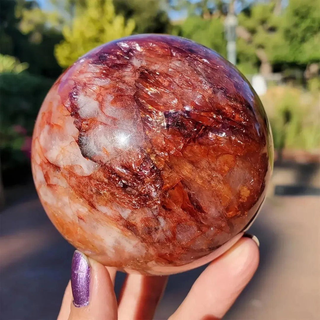 Red Hematoid Fire Quartz Sphere with fiery red and orange inclusions, held in a hand, radiating passionate energy.