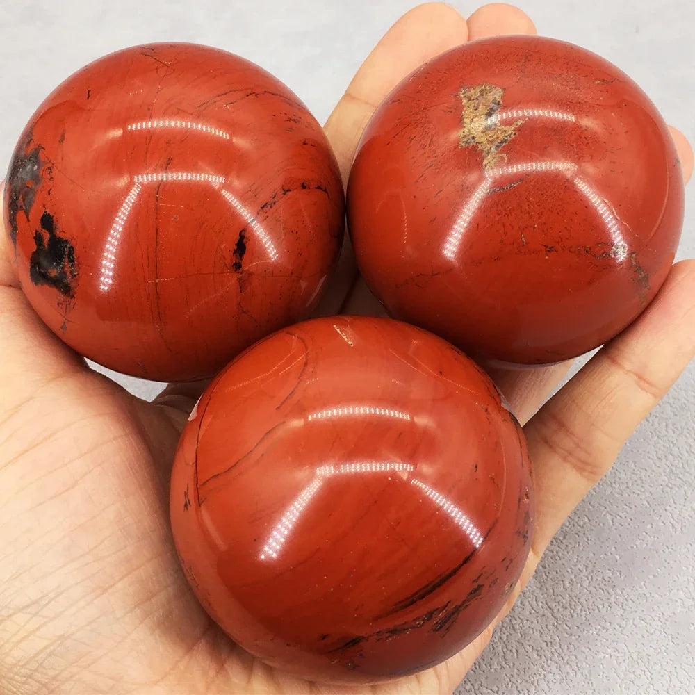 Three polished Red Jasper crystal spheres, deep brick-red with dark veins, held in a palm for grounding and vitality.