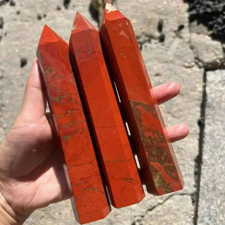 Hand holding three tall, polished Red Jasper Crystal Destiny towers with earthy red and brown tones.