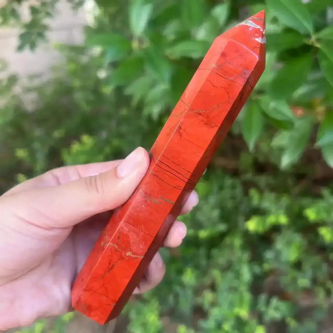 Hand holding a tall, polished Red Jasper crystal tower from Crystal Destiny, showcasing its earthy red tones and grounding energy.