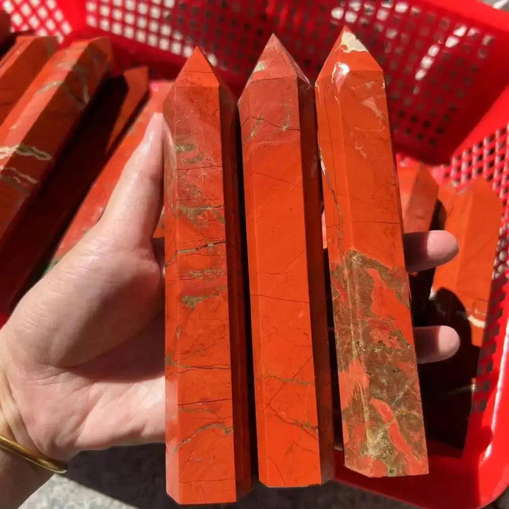 Hand holding three tall, polished Red Jasper crystal towers from Crystal Destiny, showcasing earthy red tones.