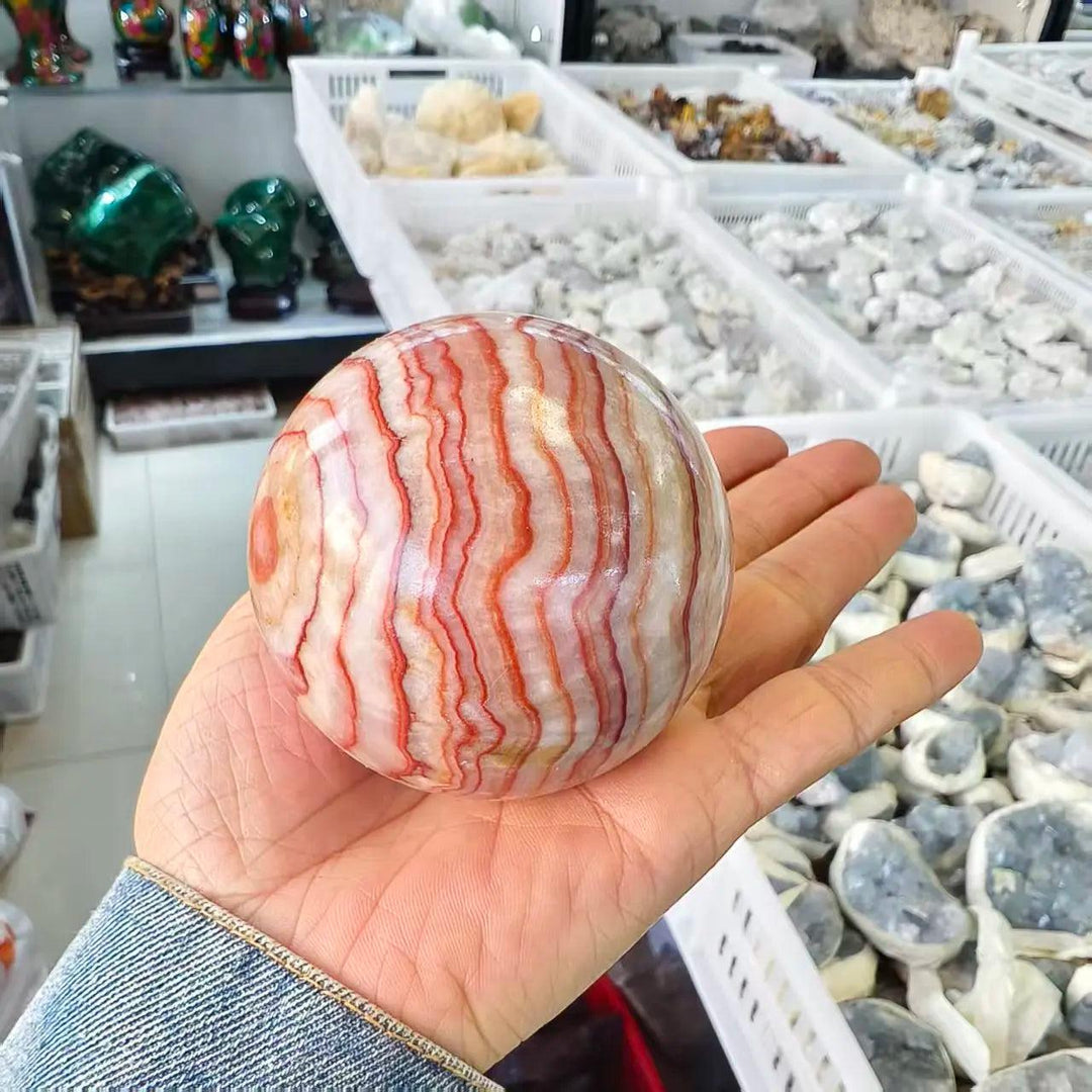 Polished natural Rhodochrosite crystal ball with vibrant red and white banded patterns for healing and home decor.
