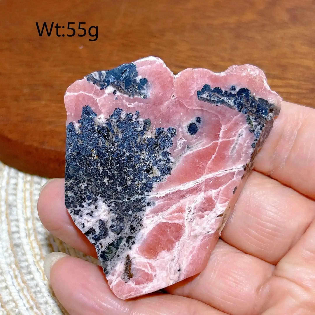 Polished Rhodochrosite raw slab with rose-pink banding and dark mineral inclusions for heart chakra healing and display.