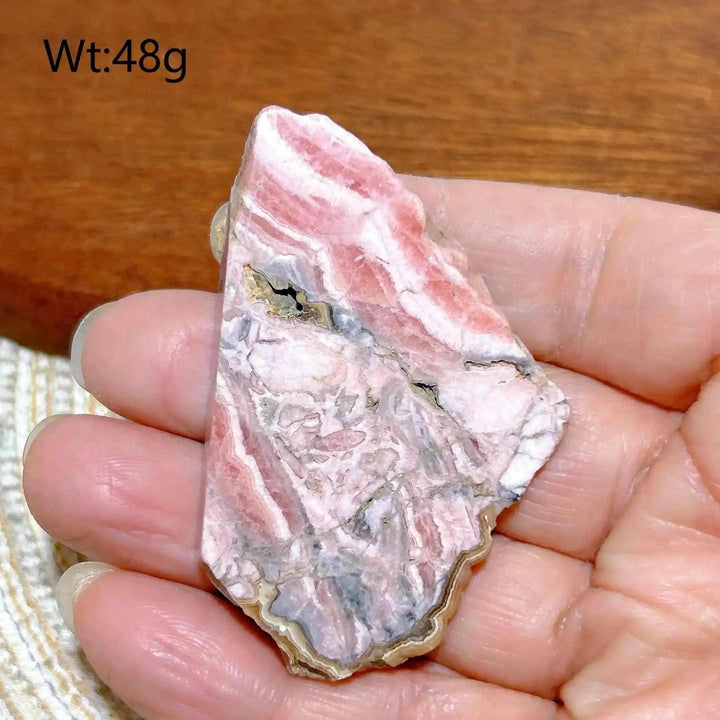 Polished Rhodochrosite raw slab with rose-pink banding for heart chakra healing and self-love, held in a hand.