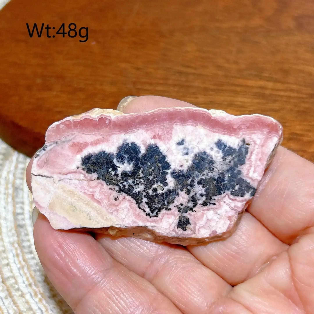 Polished Rhodochrosite raw slab featuring rose-pink banding and dark inclusions for heart chakra healing and display.