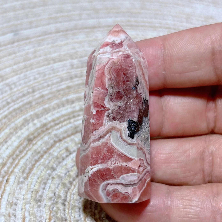Polished Rhodochrosite tower point featuring raspberry pink hues and white banding for heart chakra healing and self-love.