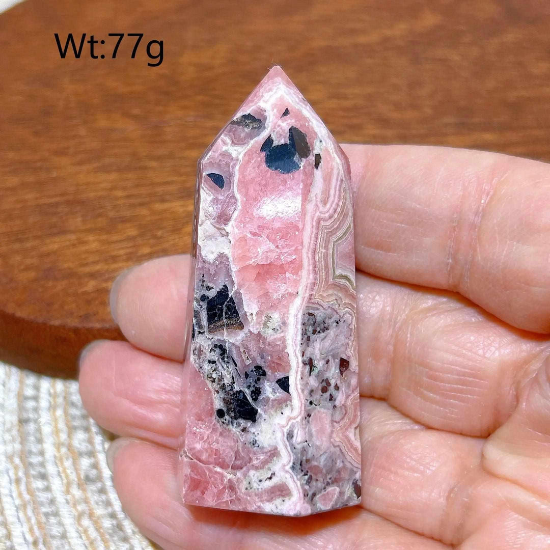 Polished 77g Rhodochrosite tower point featuring beautiful rose pink hues, white banding, and unique dark mineral inclusions.
