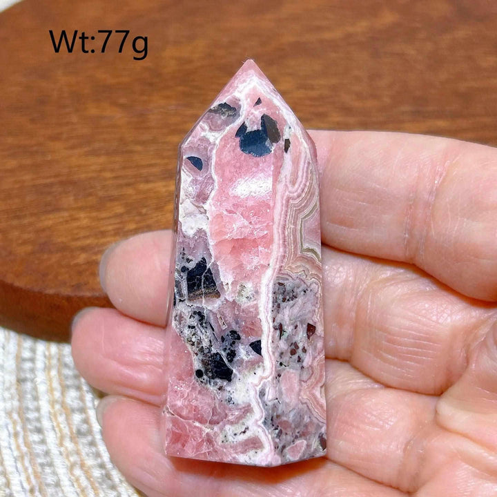 Polished 77g Rhodochrosite tower point featuring beautiful rose pink hues, white banding, and unique dark mineral inclusions.
