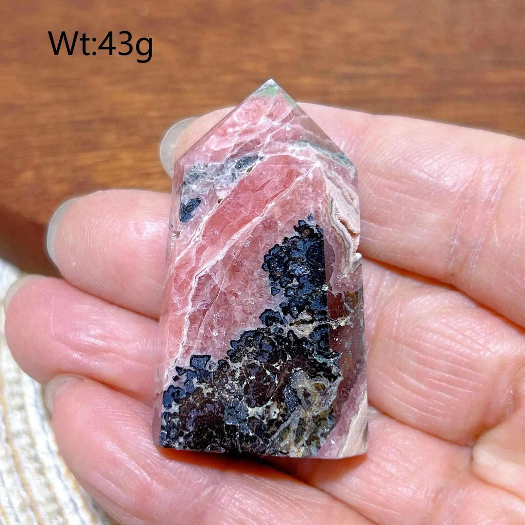 Polished Rhodochrosite tower point featuring rose pink hues, white banding, and unique dark mineral inclusions.