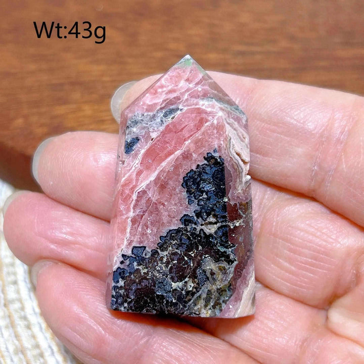 Polished Rhodochrosite tower point featuring rose pink hues, white banding, and unique dark mineral inclusions.