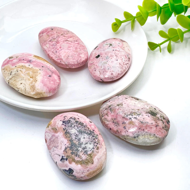 Polished natural pink Rhodonite palmstones with unique black mineral inclusions, perfect for healing and home decor.