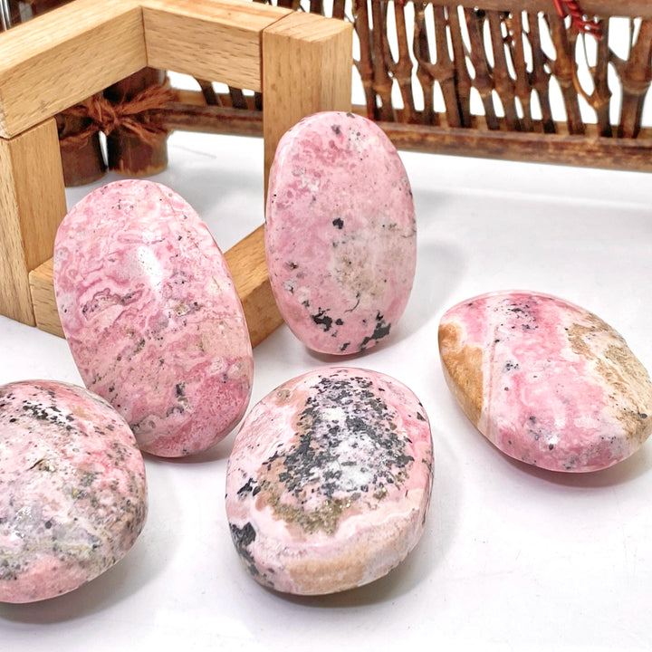 Polished natural pink Rhodonite palmstones with unique black mineral inclusions, perfect for healing and home decor.