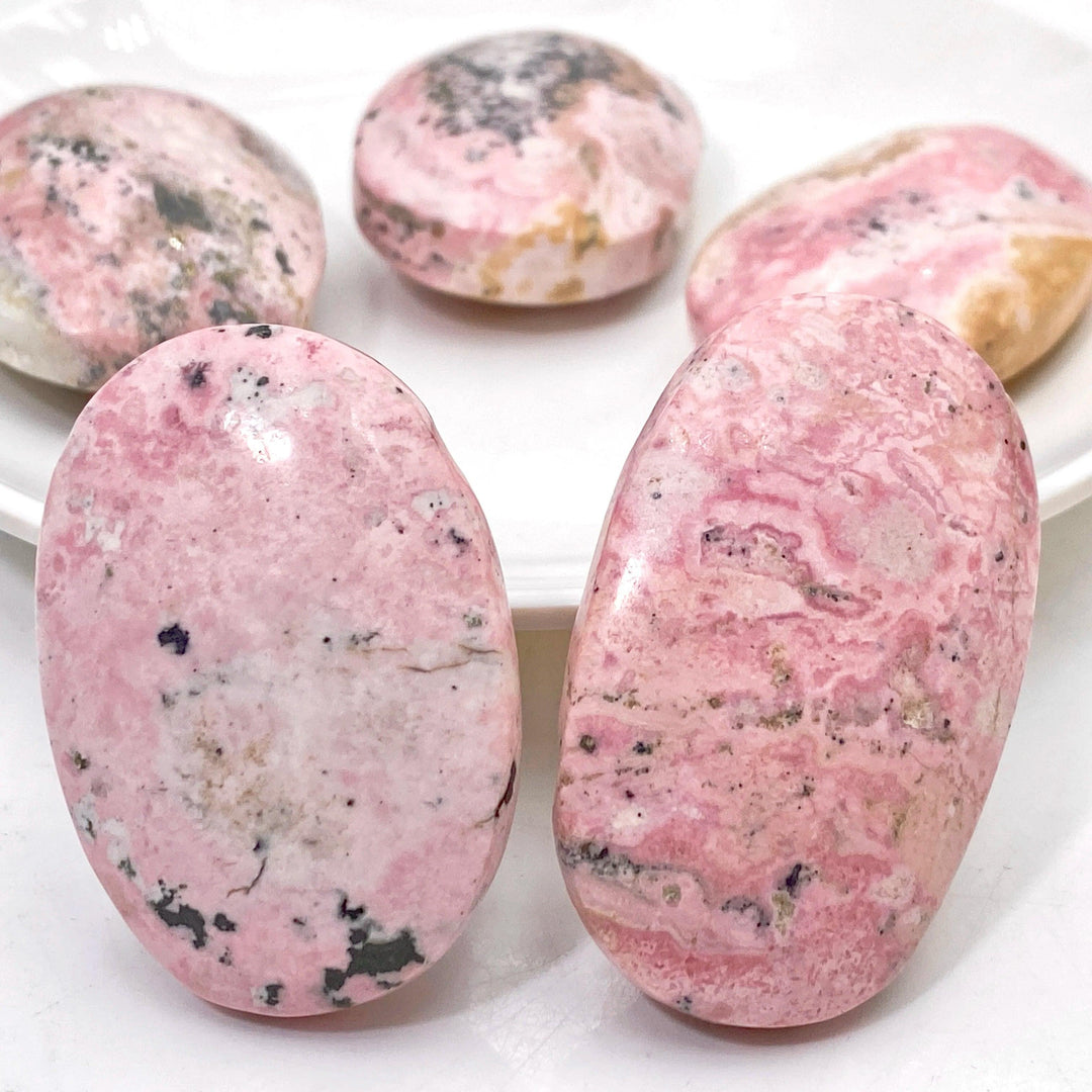 Polished natural pink rhodonite palmstones with unique black mineral inclusions, perfect for healing and home decor.