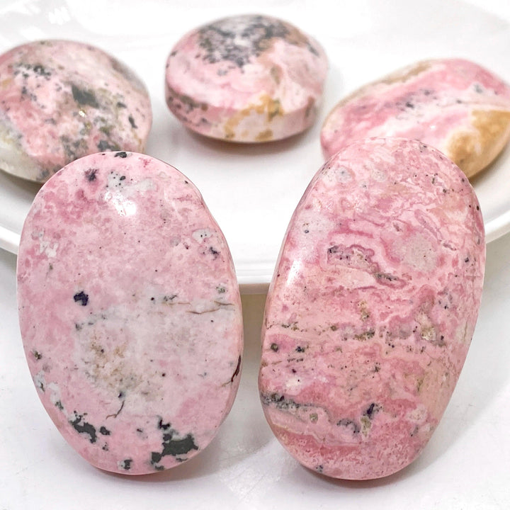 Polished natural pink rhodonite palmstones with unique black mineral inclusions, perfect for healing and home decor.