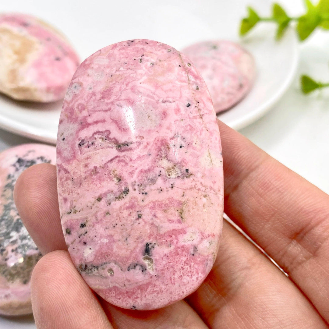 Polished natural pink Rhodonite palmstone with unique black veining, perfect for healing, meditation, or home decor.