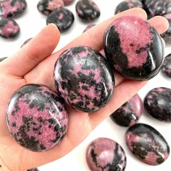 Smooth Rhodonite palm stone with pink hues and black veining, perfect for heart chakra healing and emotional balance.