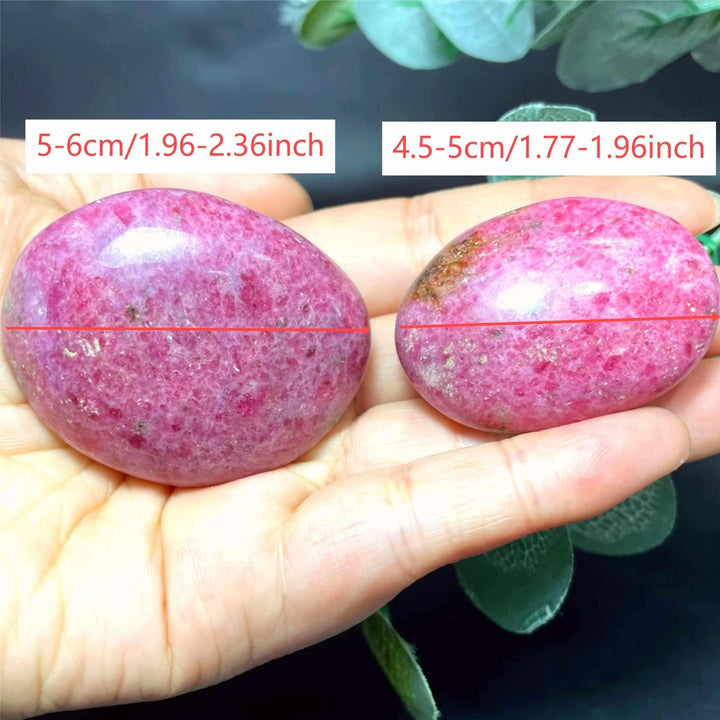 Smooth pink Rhodonite palm stones with black veining, held in hand to show size for heart chakra meditation and grounding.