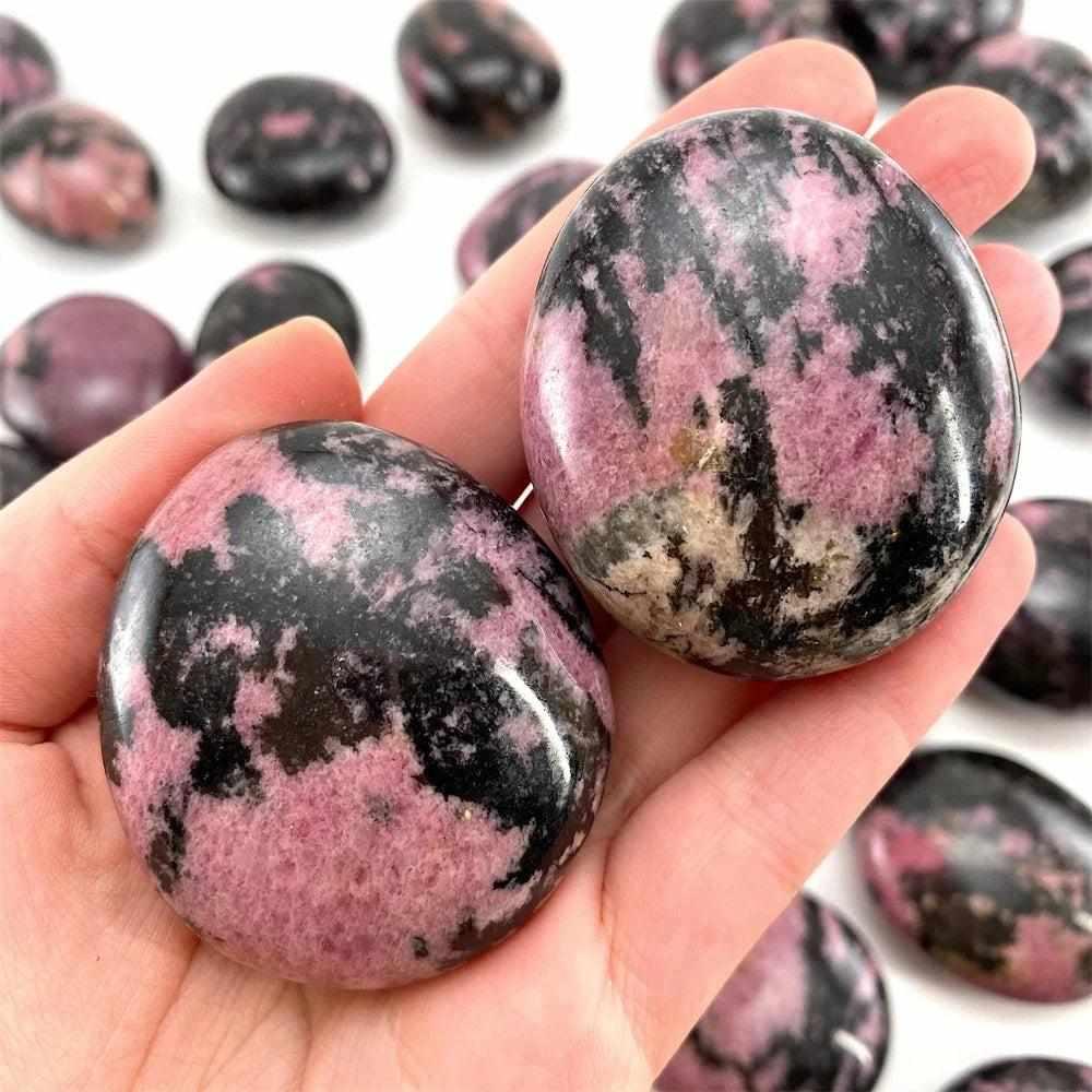 Smooth Rhodonite palm stone with vibrant pink hues and bold black veining, perfect for heart chakra healing and grounding.