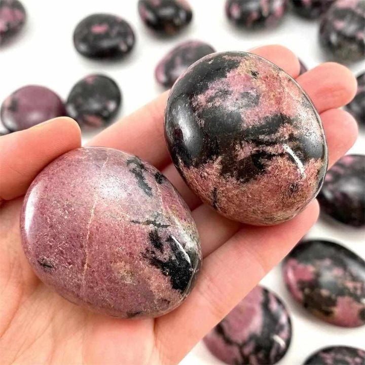 Smooth Rhodonite palm stone with pink hues and black veining, perfect for heart chakra healing and emotional balance.