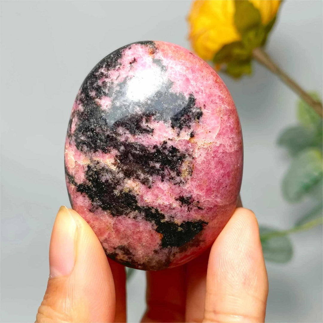 Smooth Rhodonite palm stone featuring vibrant pink hues and striking black veining for heart chakra healing and balance.