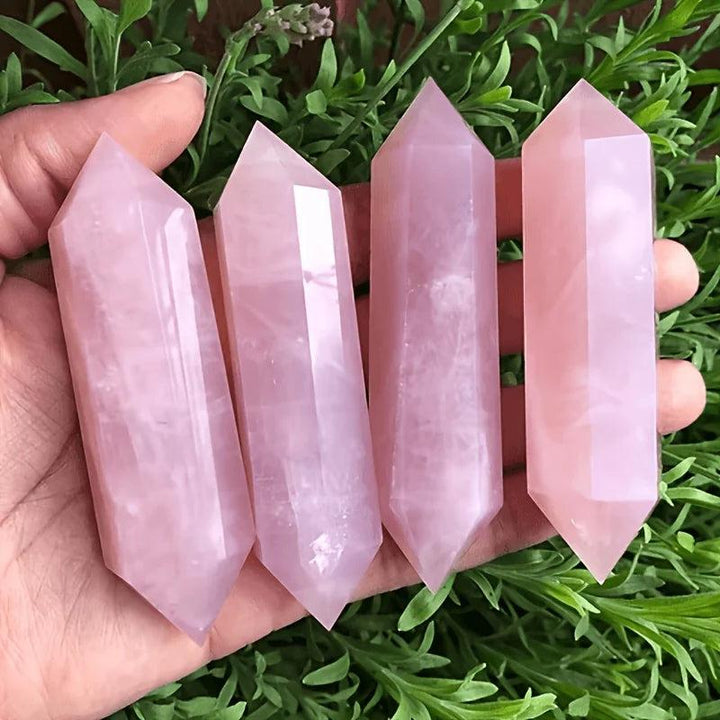 Four pink Rose Quartz Crystal Double Point Wands held in hand for heart chakra healing.