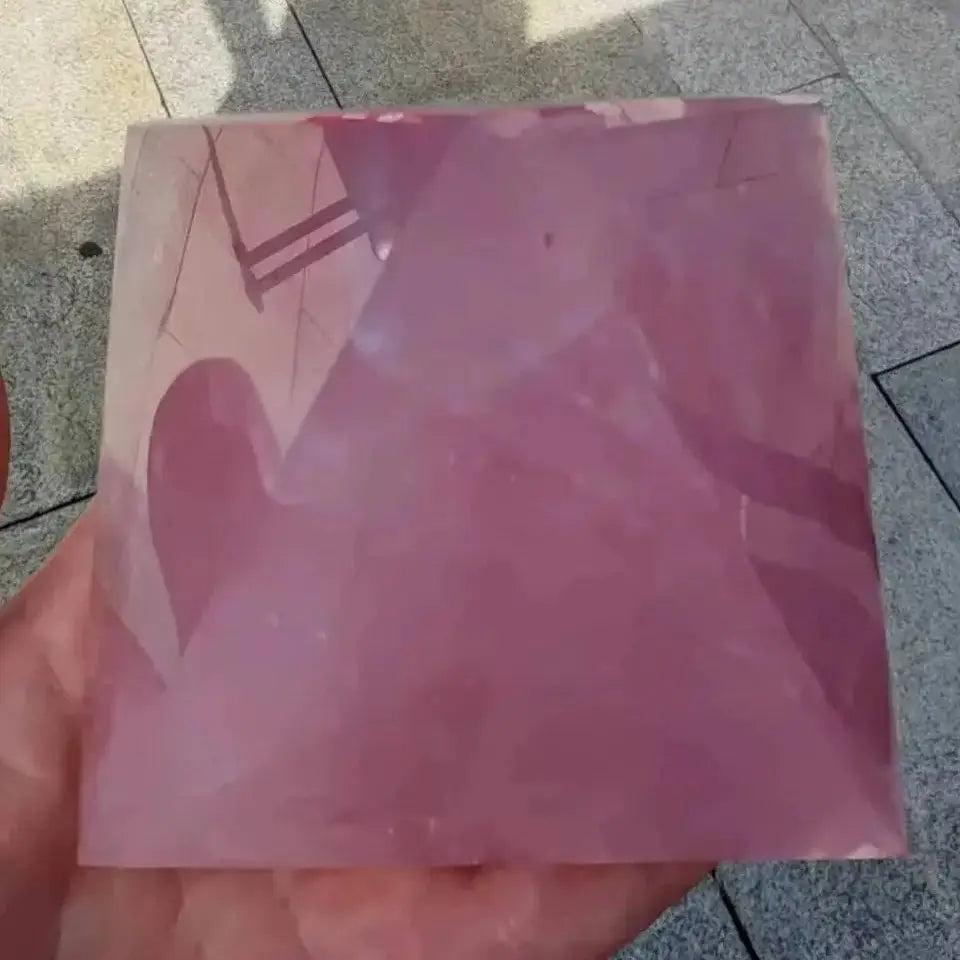 Polished rose quartz crystal pyramid, soft pink, held in a hand, reflecting light. Healing stone for love.