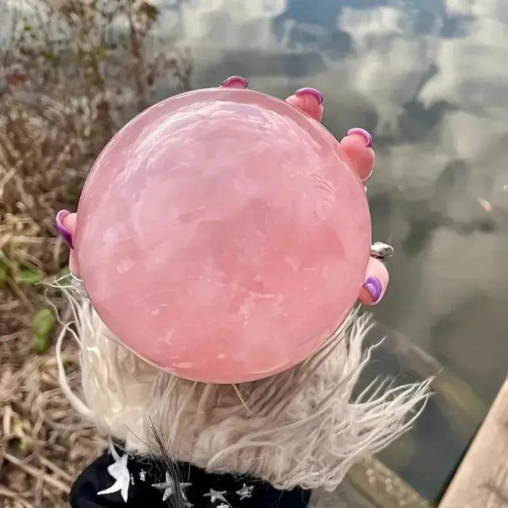 Polished Rose Quartz Crystal Sphere, a soft pink stone of unconditional love, held outdoors by a hand with purple nails.