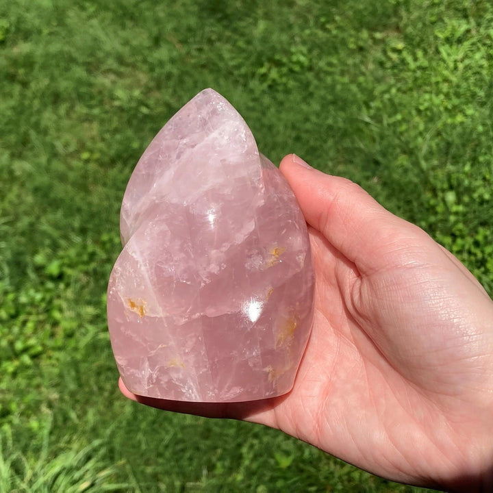 Hand holding a polished, soft pink Rose Quartz crystal torch tower with a flowing point.