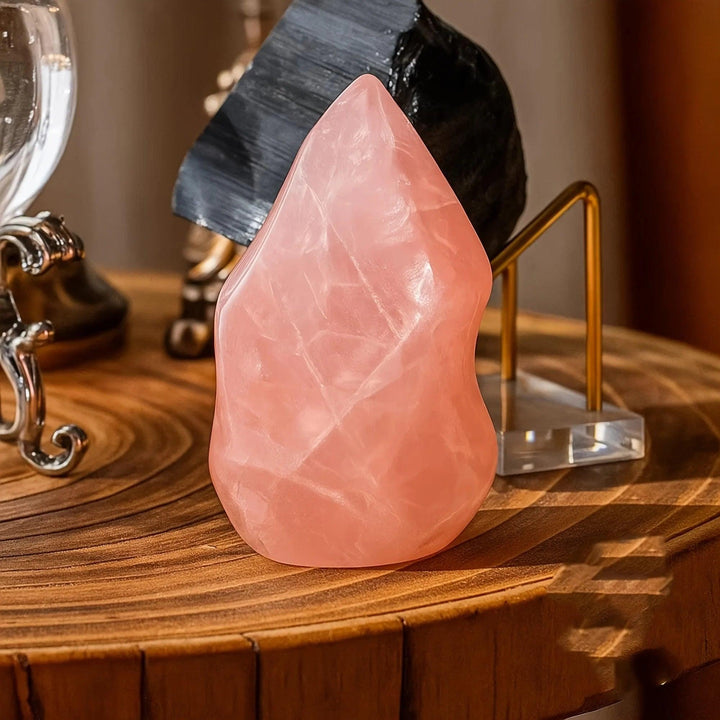 Polished rose quartz crystal torch tower, soft pink, with a tapered point and flat base on a wooden surface.