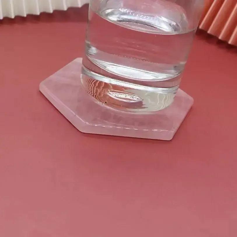 Polished Rose Quartz hexagon coaster from Crystal Destiny, holding a glass of water on a pink surface.