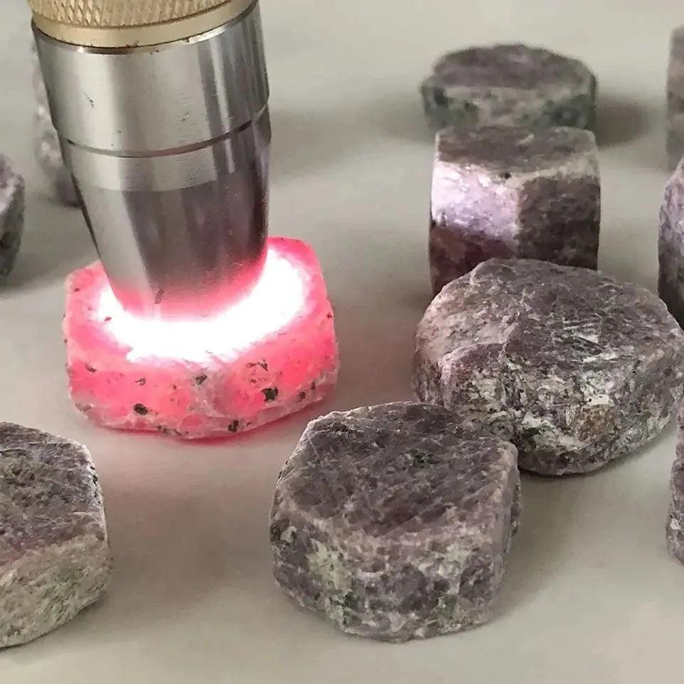 Vibrant raw Ruby Corundum crystal glowing with deep red light, surrounded by natural rough stone specimens.