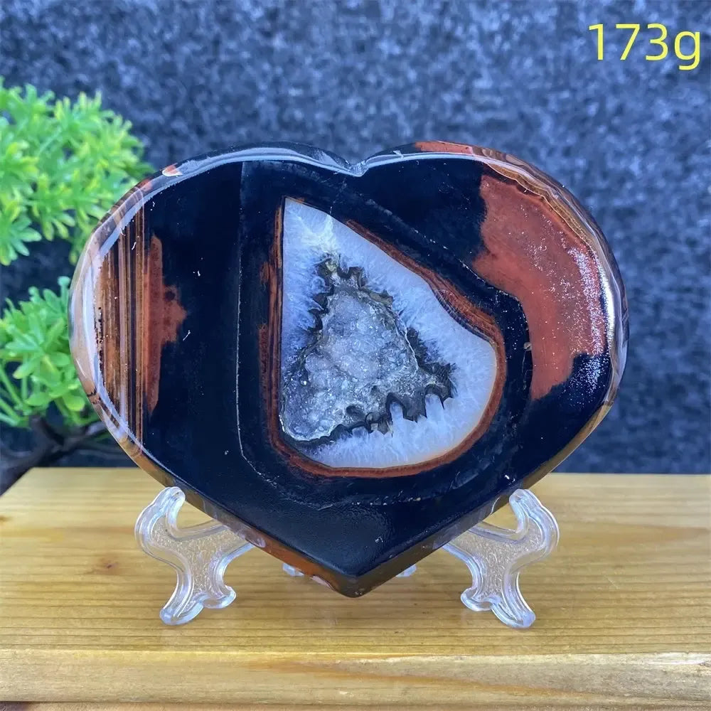 Heart-shaped black and red agate geode with sparkling white crystal cave, 173g, on a stand.