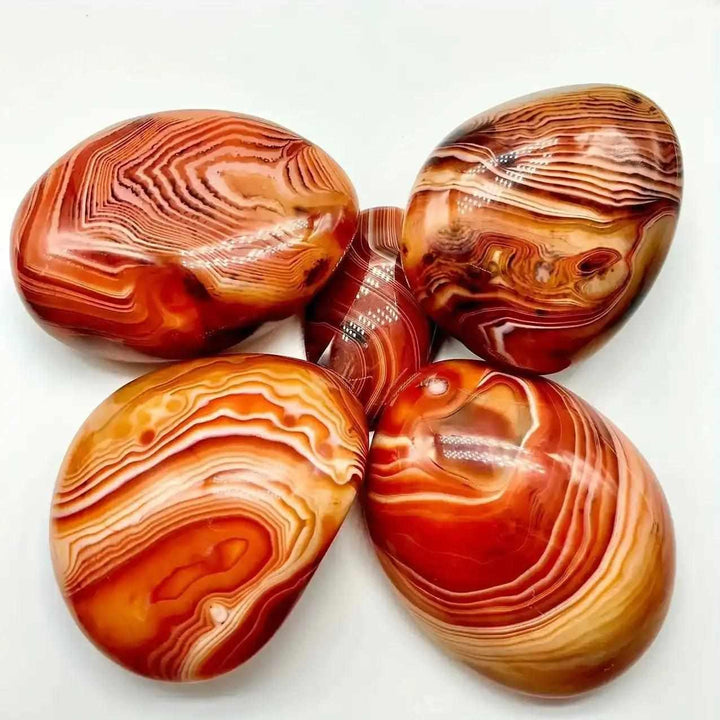 Polished Sardonyx palm stones with smooth, banded patterns of reddish-brown, honey, and white for grounding and strength.