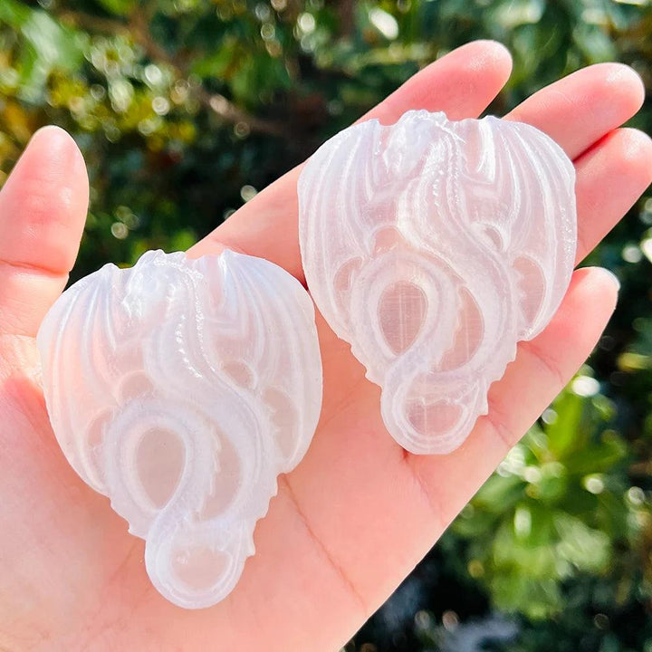 Two glowing Selenite Crystal Carved Flying Dragons, milky white with intricate wings, held in a hand.