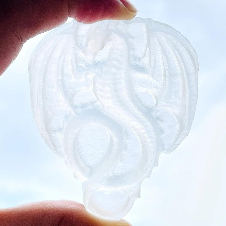 Selenite Crystal Carved Flying Dragon, glowing milky white, held against a bright sky.