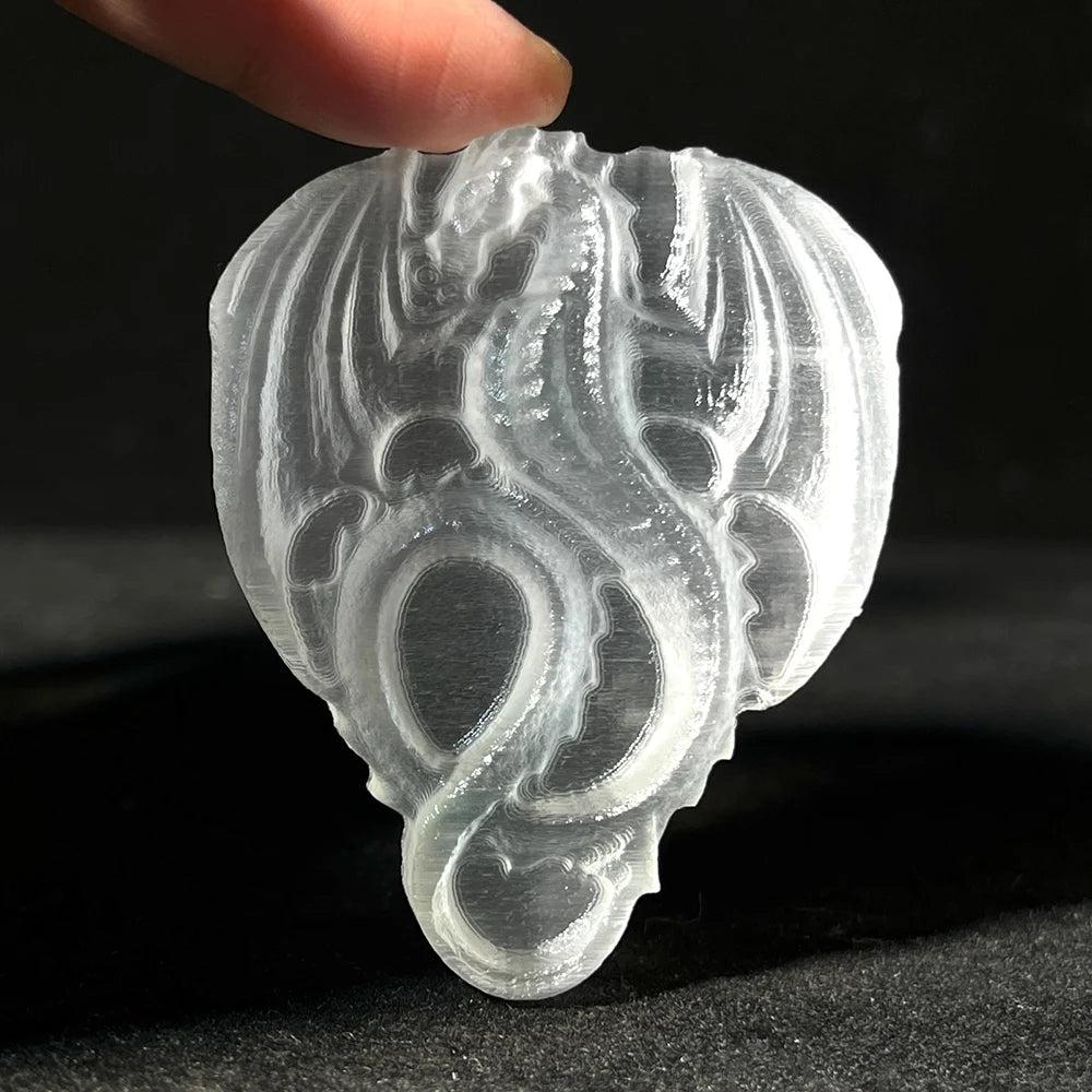 Translucent selenite crystal carved into a flying dragon, held by fingertips, for cleansing and peace.