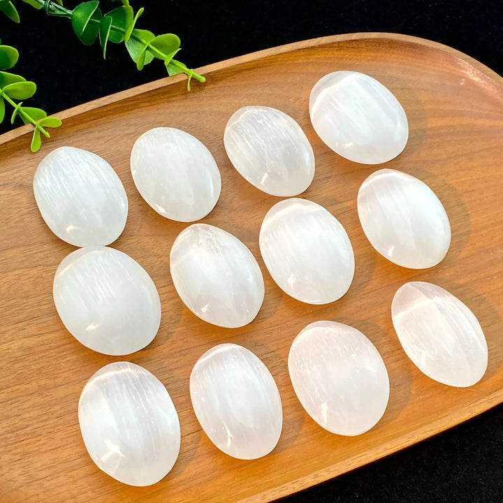 Polished natural white selenite palm stones on a wooden tray, perfect for healing, meditation, and home decor.