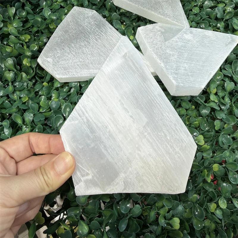 Selenite Crystal Flat Slab Charging Plate for Cleansing. Luminous white selenite slab held over green foliage.