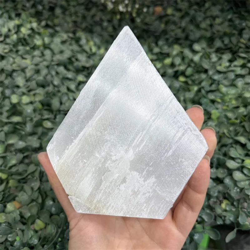 Luminous white Selenite Crystal Flat Slab Charging Plate for cleansing, held against green foliage.