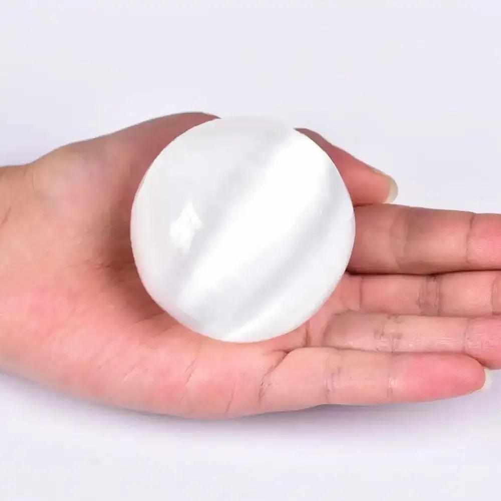 Polished white Selenite crystal sphere with a silky glow, held in hand for peaceful energy and Crown Chakra cleansing.