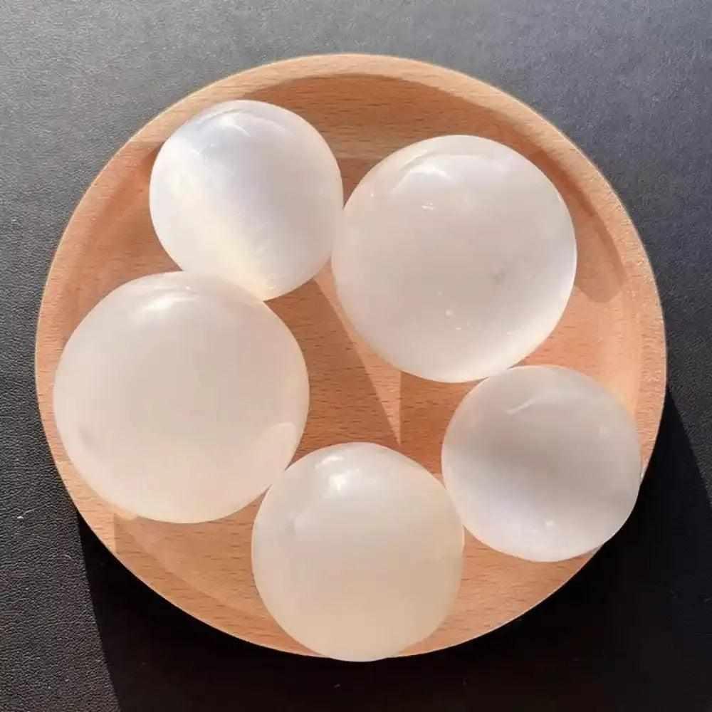 Polished white Selenite crystal spheres on a wooden tray for Crown Chakra cleansing and peaceful, glowing energy.