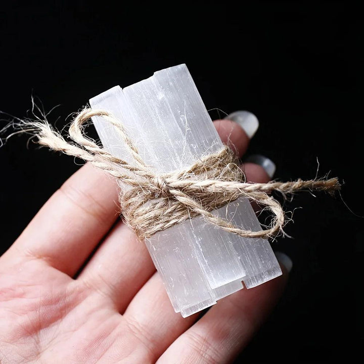 Hand holding a bundle of natural white Selenite Crystal Wands, raw gypsum sticks tied with twine.