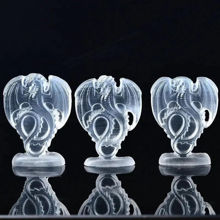 Three luminous white selenite fire dragon carvings from Crystal Destiny, reflecting on a dark surface.
