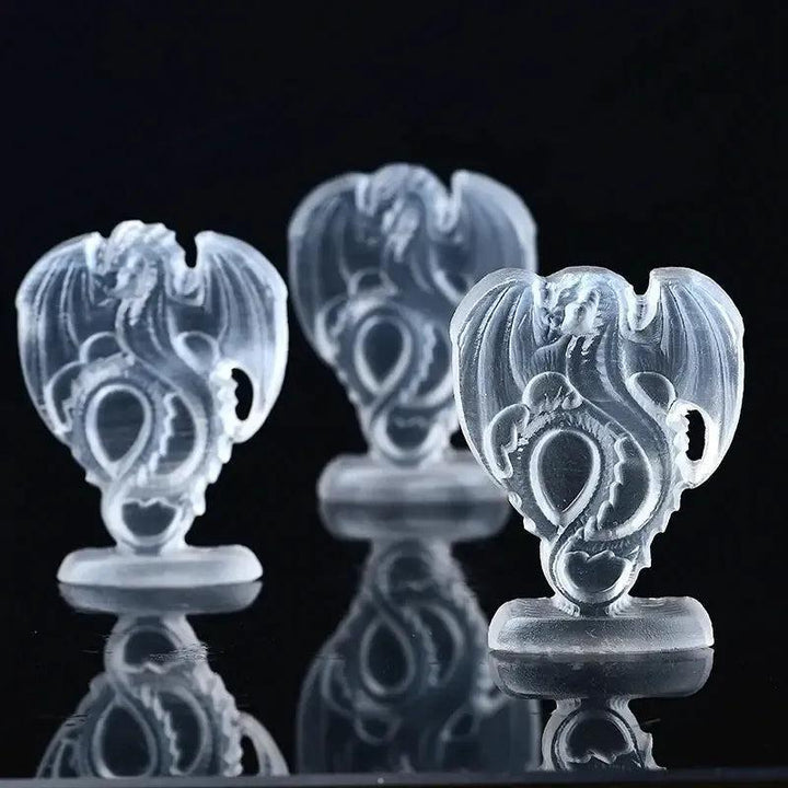 Three translucent white selenite fire dragon carvings from Crystal Destiny, reflecting light on a dark surface.