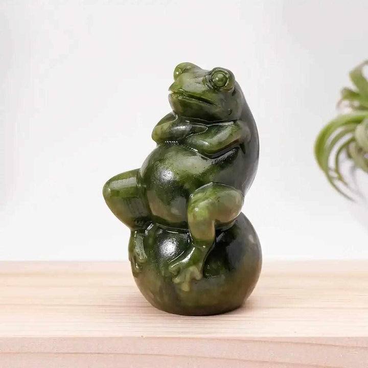 Polished Serpentine Jade frog carving seated on a round ball, featuring mottled forest and olive green tones.