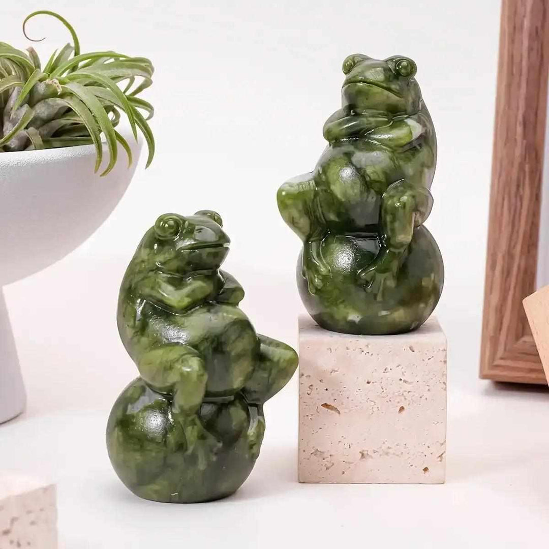 Two polished Serpentine Jade frog carvings seated on round balls, featuring mottled forest and olive green tones.